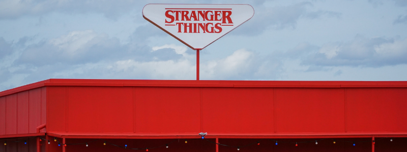 Un insegna bianca con scritto "Stranger Things" è posizionata sul tetto di un edificio rosso decorato con lucine di natale