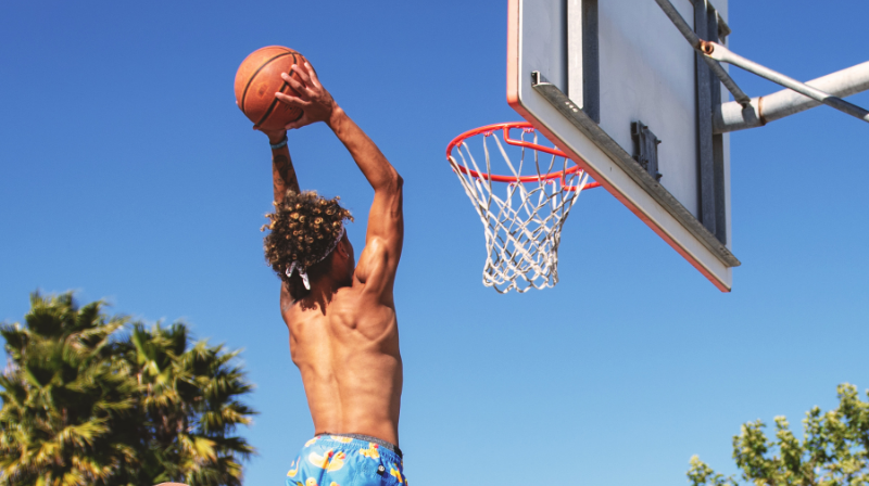 Giocatore di basket salta a torso nudo con la palla in mano, pronto per fare canestro