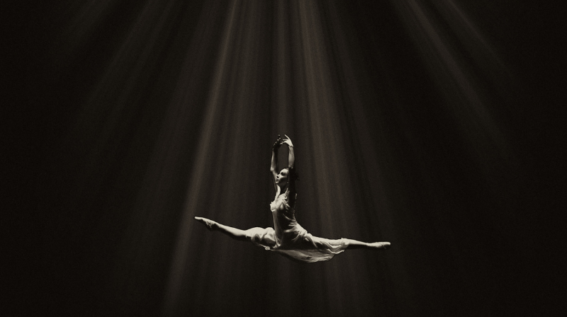 Ballerina che balla sospesa per aria con una luce filtrata che la illumina dall'alto
