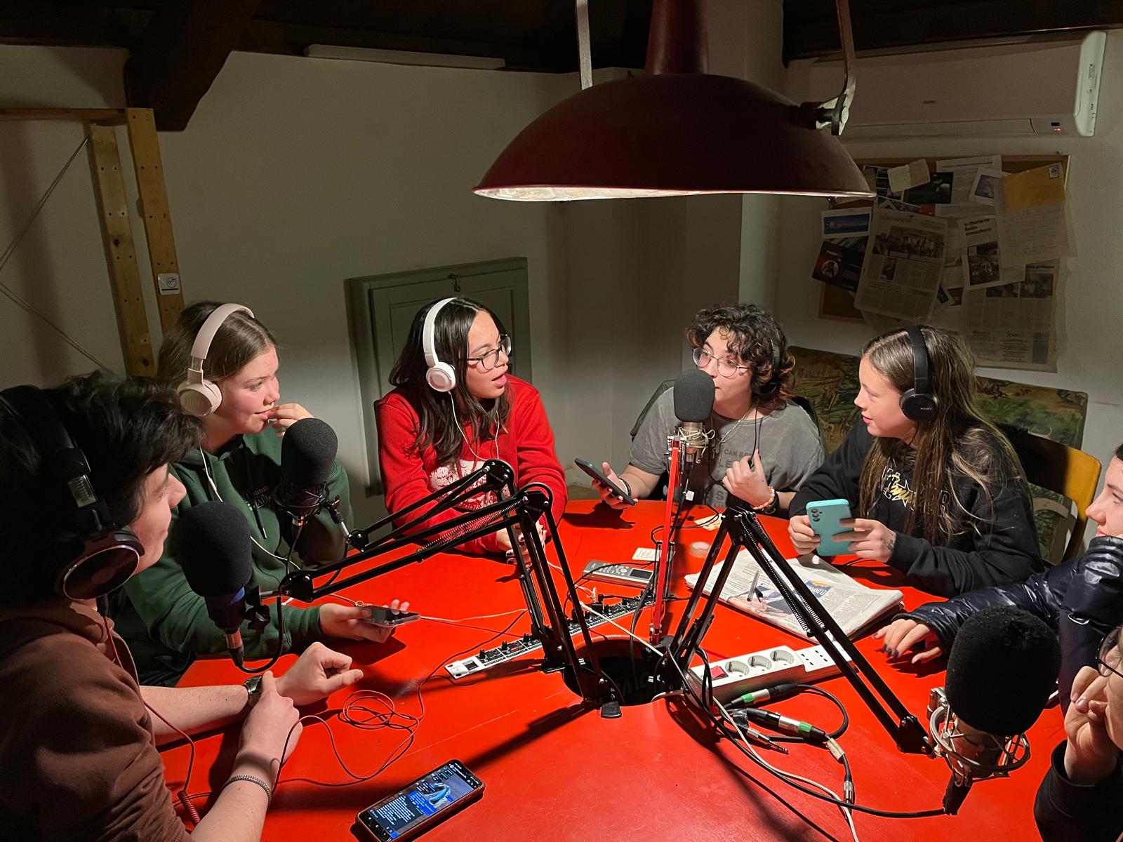 Puntata di radio Un gruppo di ragazzi registra una trasmissione radiofonica attorno ad un tavolo rosso