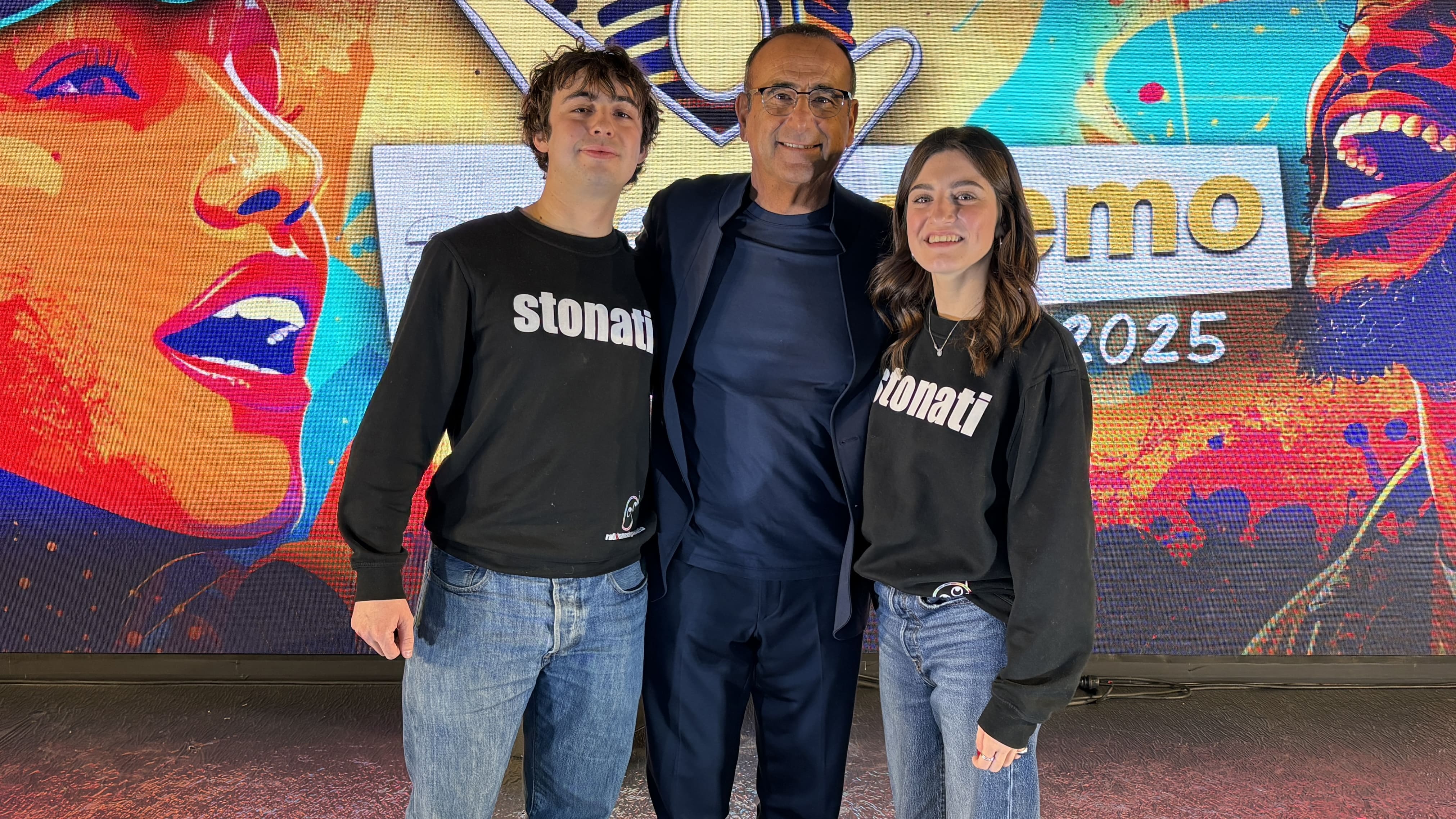 Foto del conduttore del Festival Carlo Conti insieme a due speaker di Radioimmaginaria con addosso la felpa degli STONATI